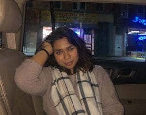 A picture of maliha who has dark hair sitting in a car, smiling.