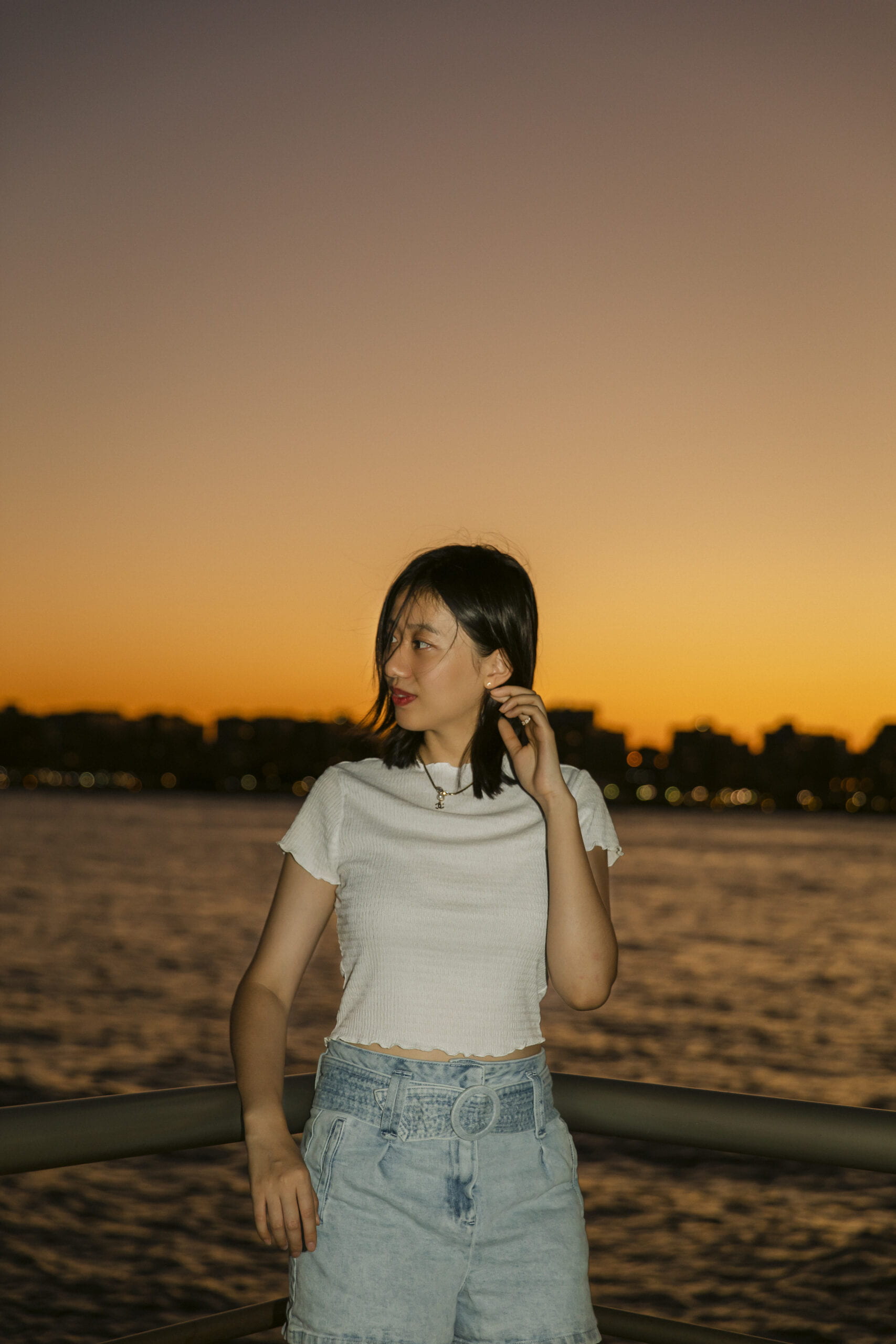 a photo of Cyrene taken in front the river by sunset; She's wearing a white top and a jean short.