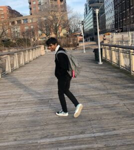 A brown male wearing all black with his head turned back as he's walking away from the camera.