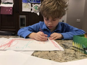 Young child sitting at a table drawing a picture with crayons. 