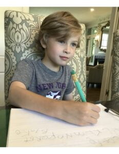 Young child sitting at a table writing with a pencil and paper.