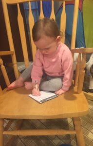 Toddler sitting on a rocking chair drawing with a crayon. 