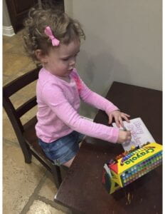 Toddler siting at a small table drawing with crayons.