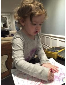 Toddler sitting at a table coloring with crayons.